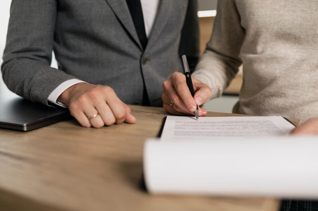 Close up of male hand singing paperwork next to man in a suit