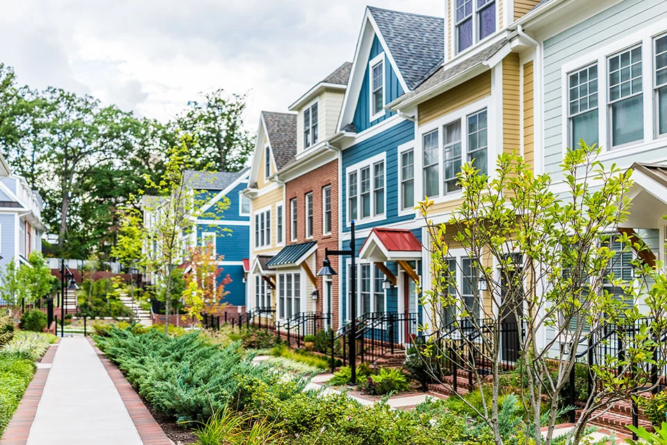 Exterior daytime view of a row of colorful multi-story townhouses featuring a landscaped pedestrian walkway in the foreground.